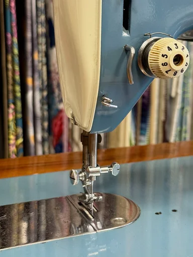 Détail d'une machine à coudre Sigma bleue : tension du fil et pied-de-biche